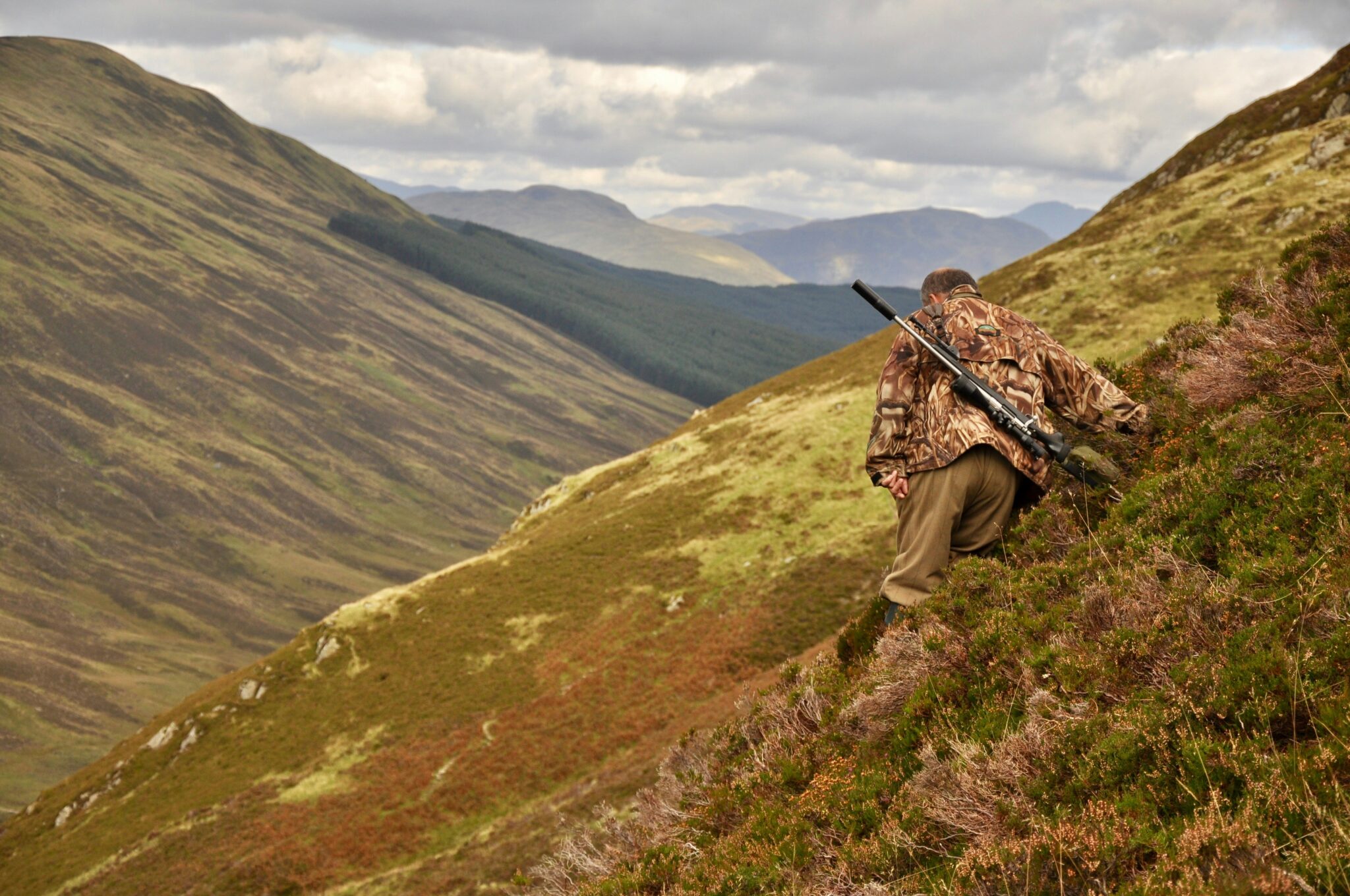 Hunter with a rifle climbing a steep mountain slope on a guided hunting outfitter trip